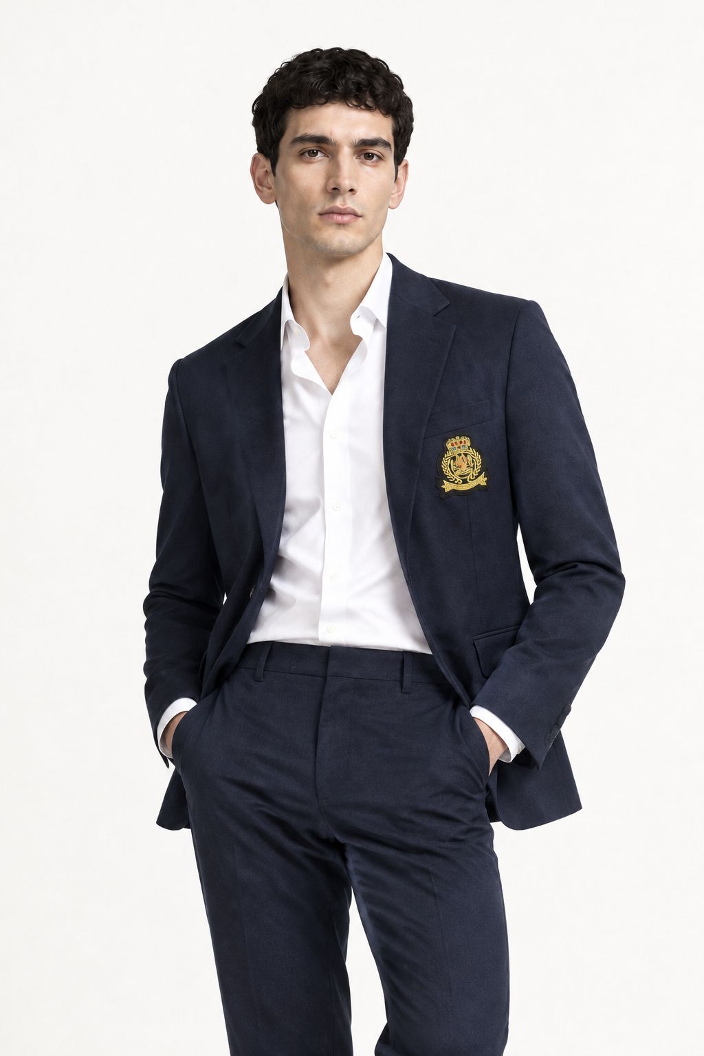 Blazer homme marine à écusson porté ouvert sur une chemise blanche, mains dans les poches